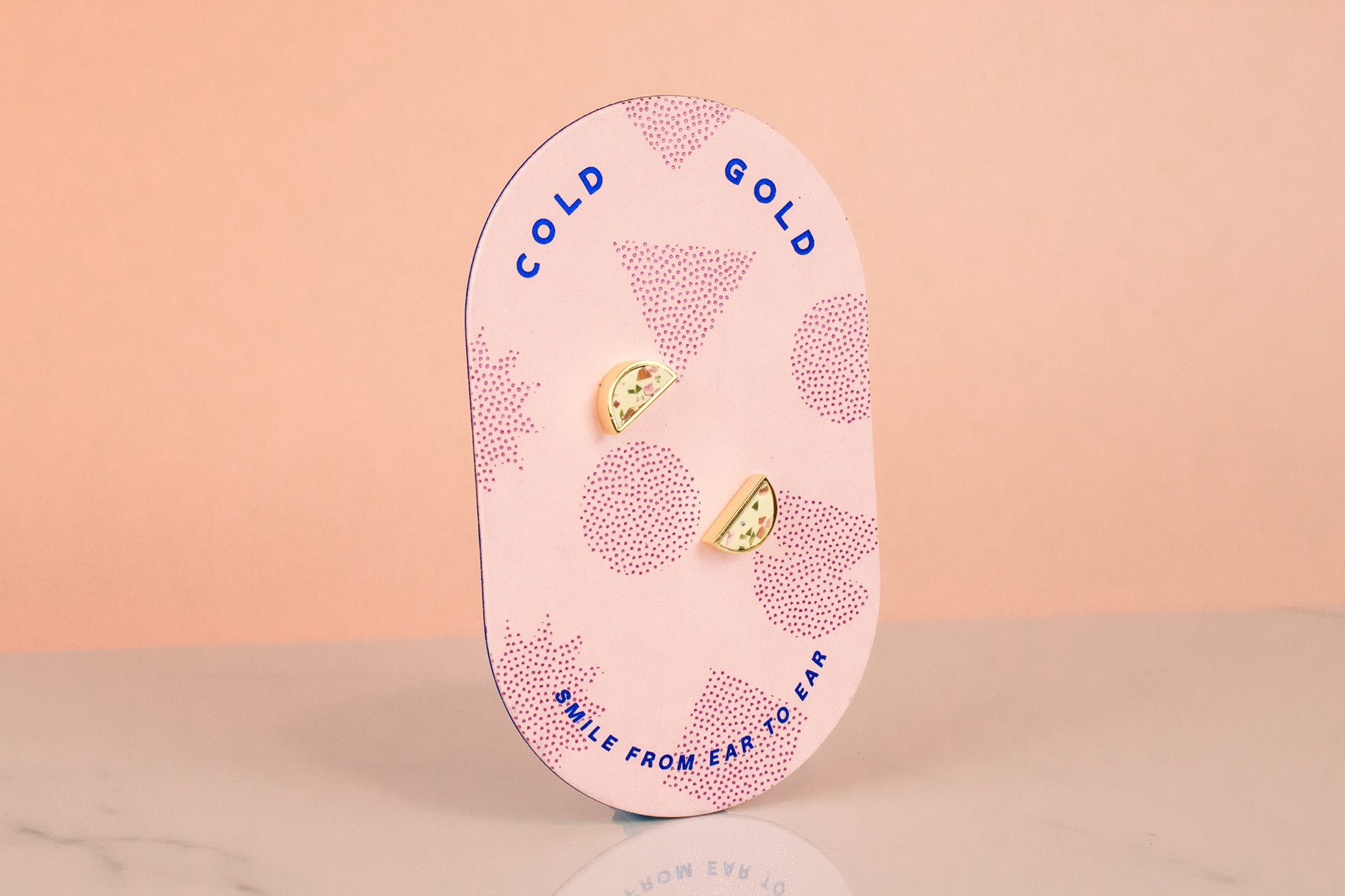 pair of gold semicircle stud earrings in terazo style on cold gold branded card