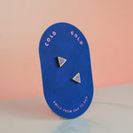 a bright blue card holding and showing a pair of gold and lavender geometric triangle earrings with 14k gold plated posts