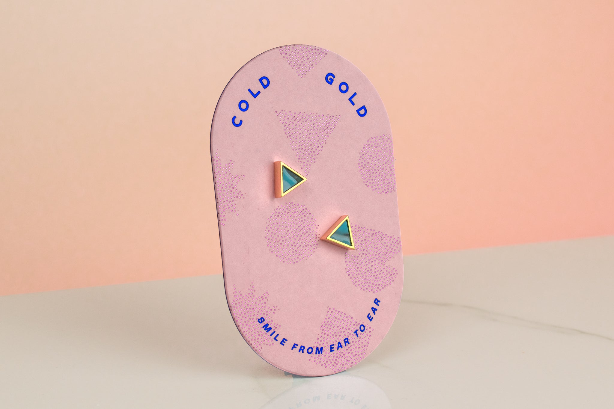 a bubblegum pink card showing a tiny triangle earring set in clay marbled to look like aquamarine crystal gemstone