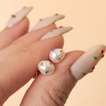 close up of a hand holding a pair of baroque pearl earrings adorned with colorful crystal gemstones