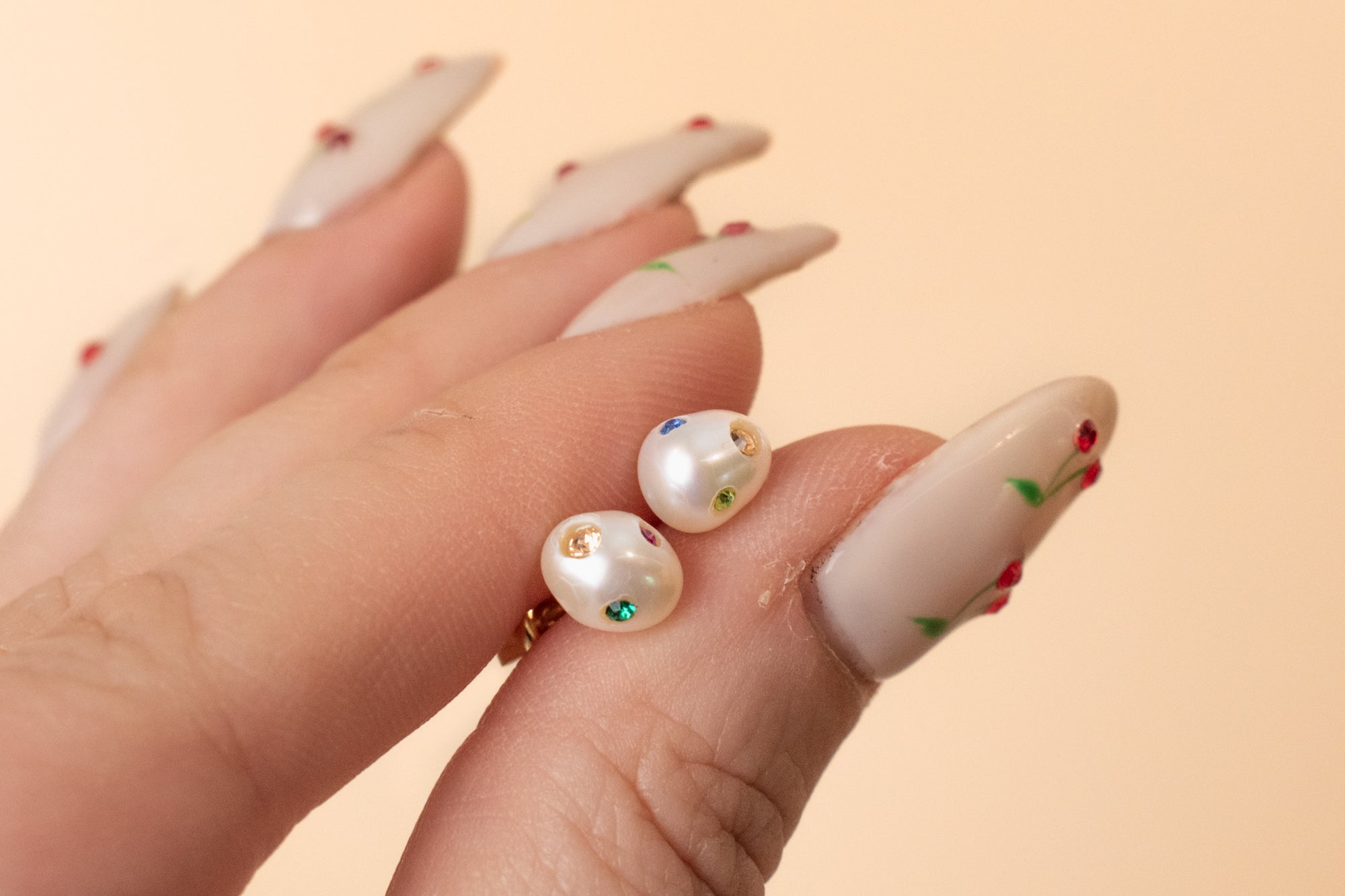 close up of a hand holding a pair of baroque pearl earrings adorned with colorful crystal gemstones