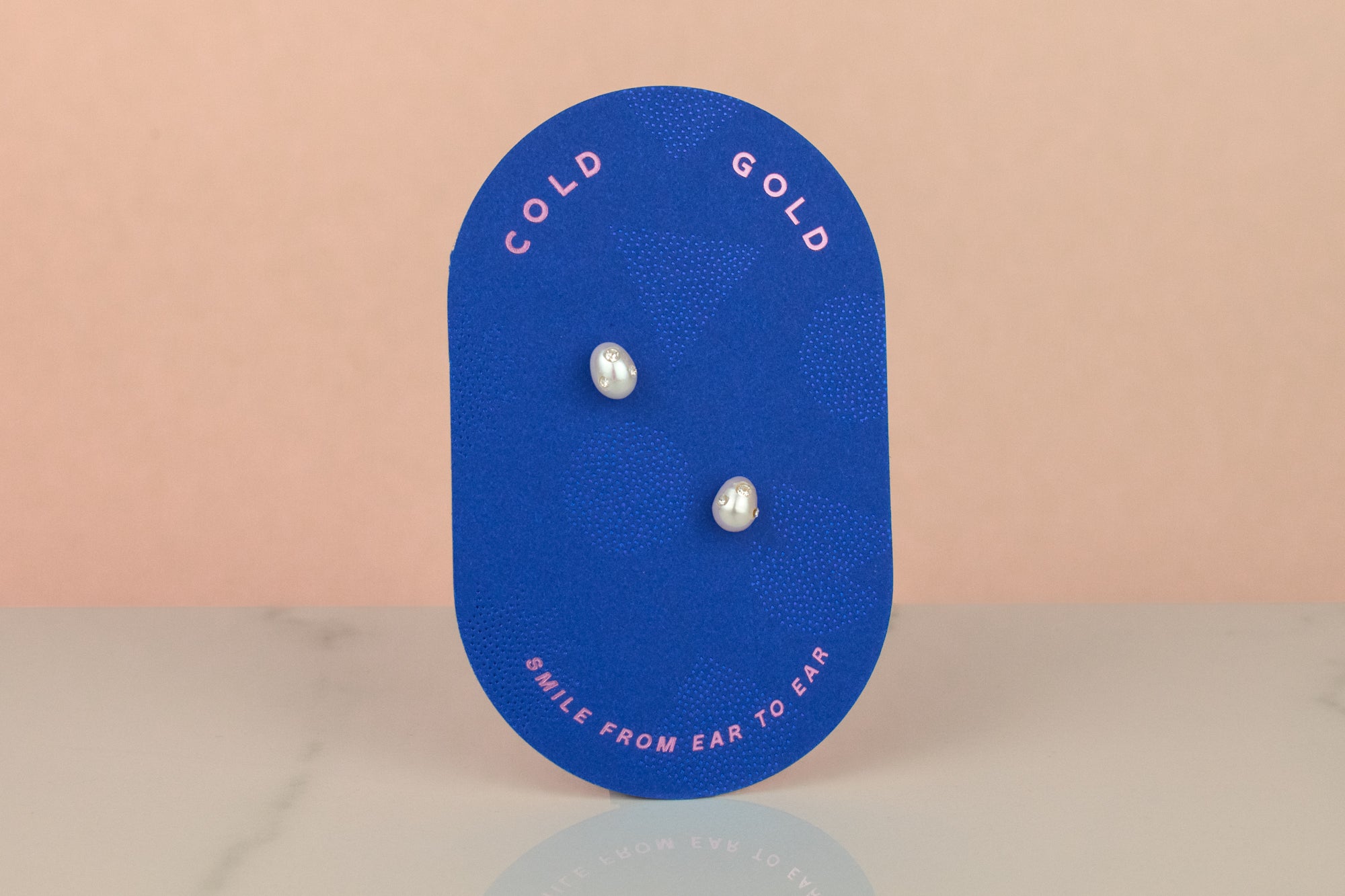 pair of bejeweled baroque pearl earrings on a cold gold branded earring card