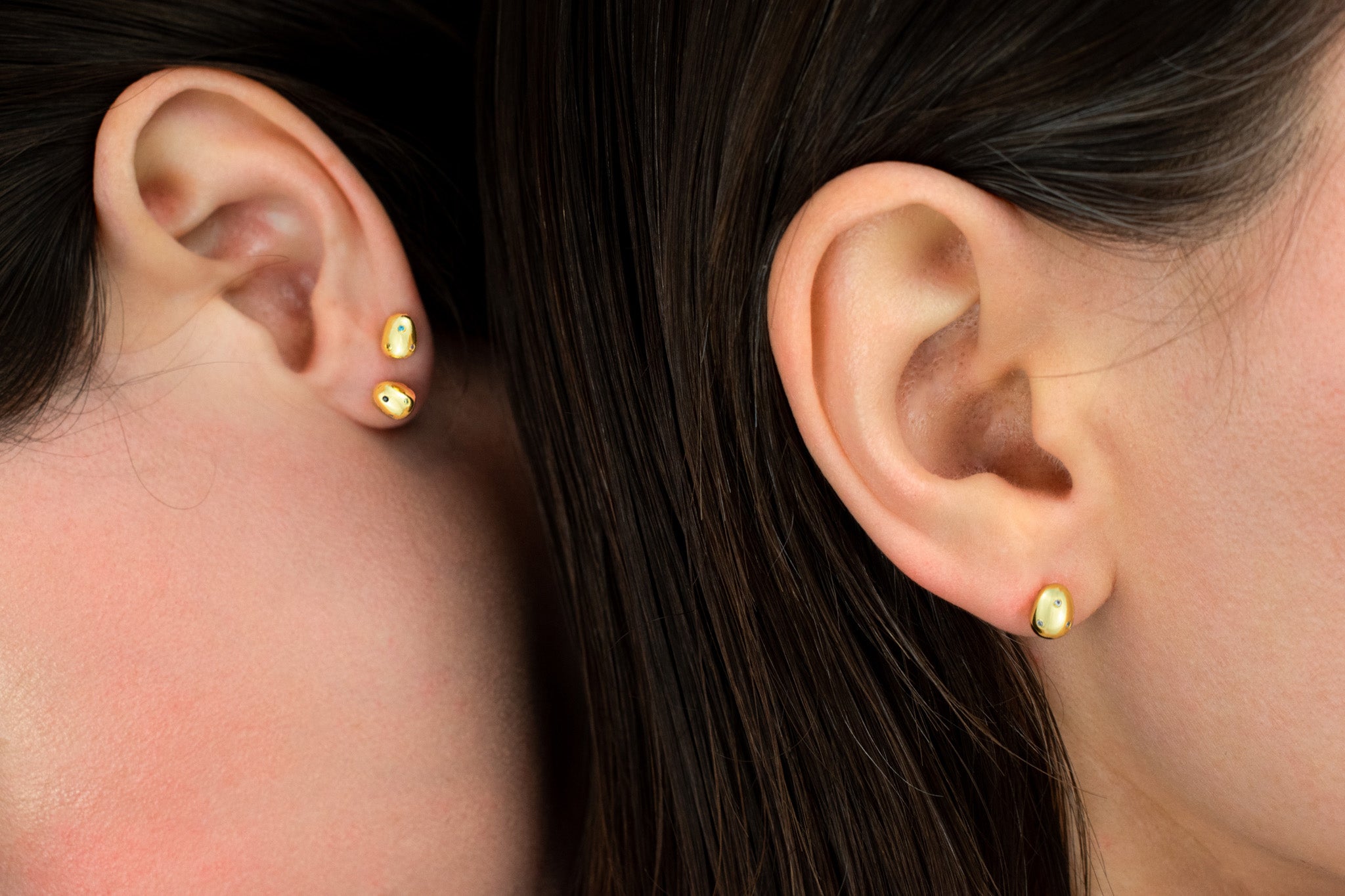 close up of two models wearing 6mm modern gold pearl stud earrings encrusted with micro CZ gemstones