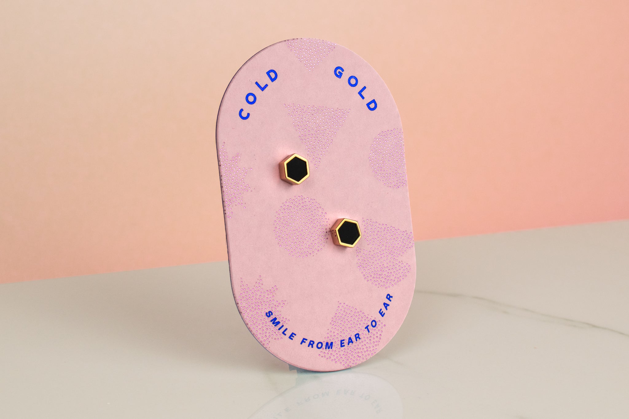 pink backer card displaying matte black hexagon gold plated earrings