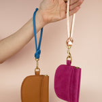 hand displaying two leather card case wristlets: magenta pink and caramel brown