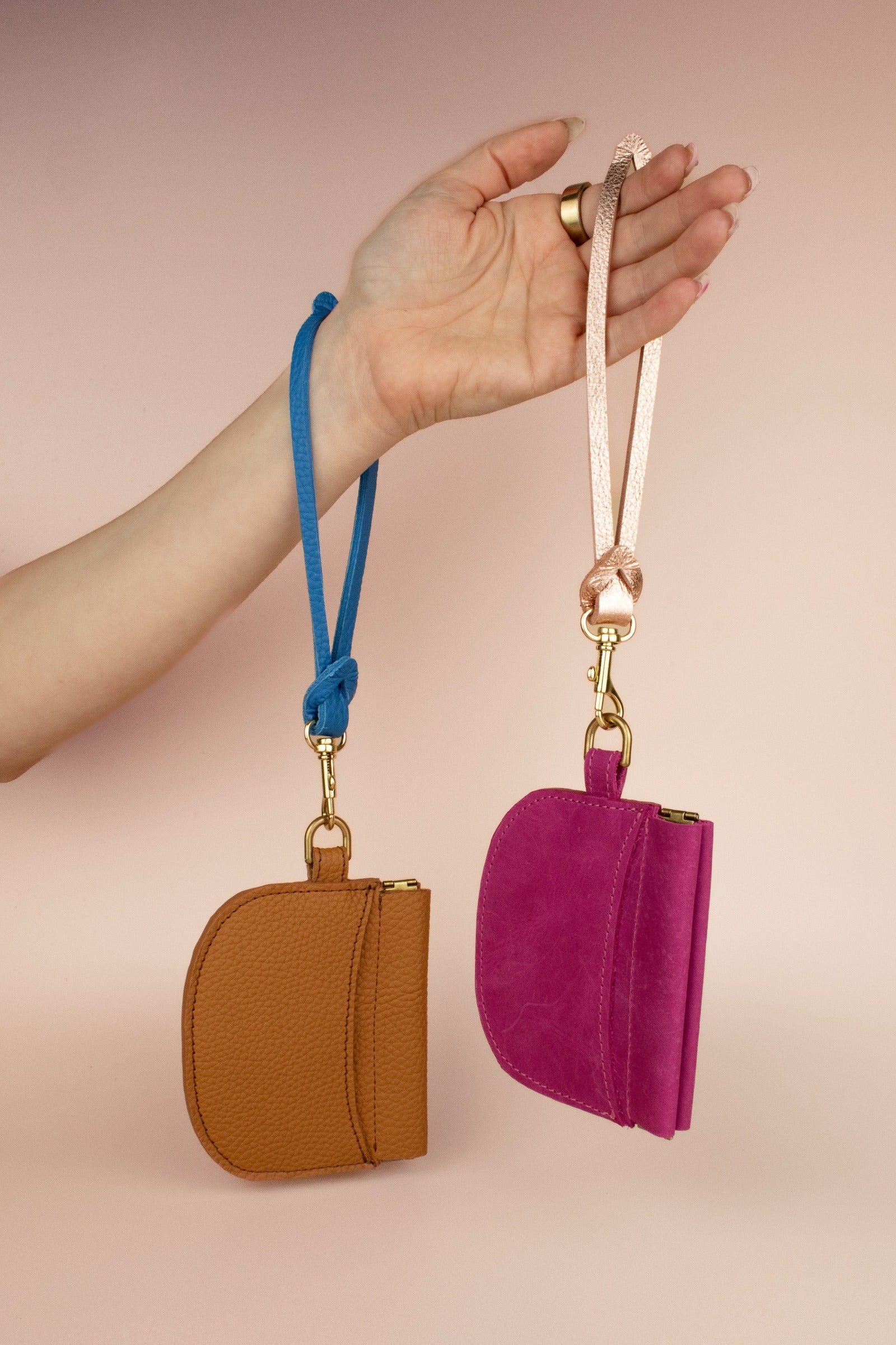 hand displaying two leather card case wristlets: magenta pink and caramel brown