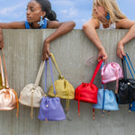 two models hanging assorted colorful mini leather bucket bags with ruched drawstring closure