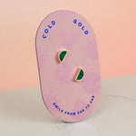 hand holding a pair of tiny gold studs on a pink geometric packaging card