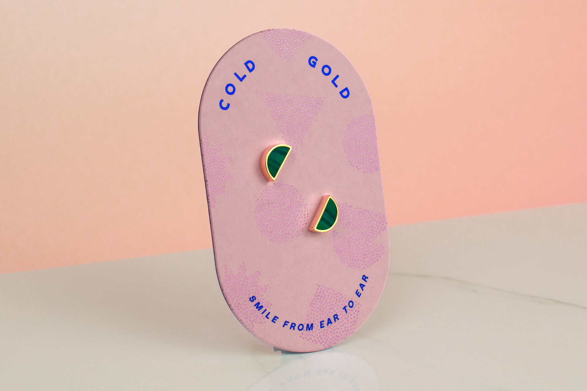 hand holding a pair of tiny gold studs on a pink geometric packaging card