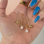 a hand holds a pair of gold freshwater baroque pearl drop earrings