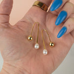a hand holds a pair of gold freshwater baroque pearl drop earrings