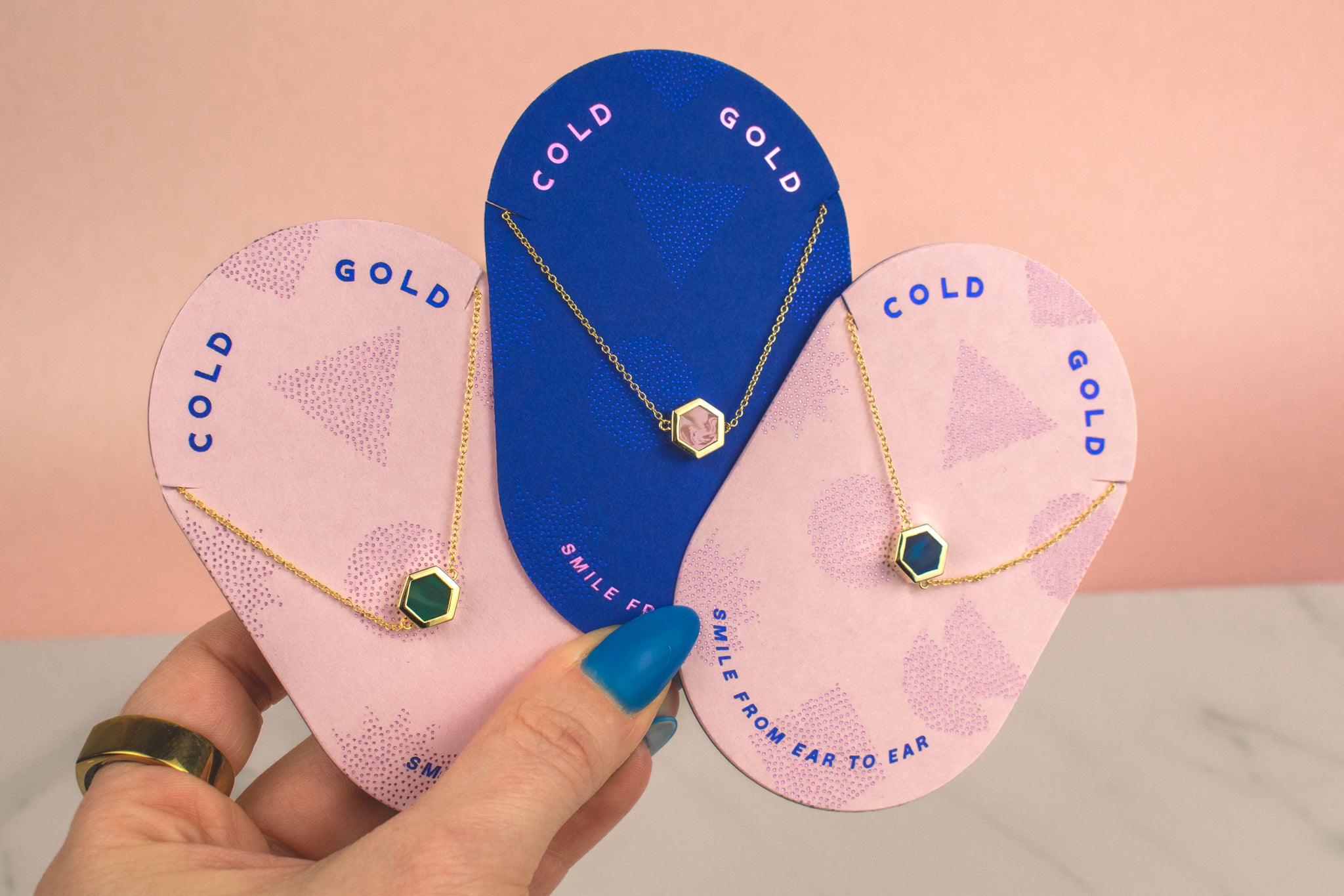 pink pill shaped cold gold cards displaying three 14k gold geo chain gemstone inspired necklaces in emerald, sapphire, and rose quartz