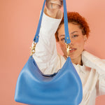 model holding up blue leather shoulder bag with convertible silhouette