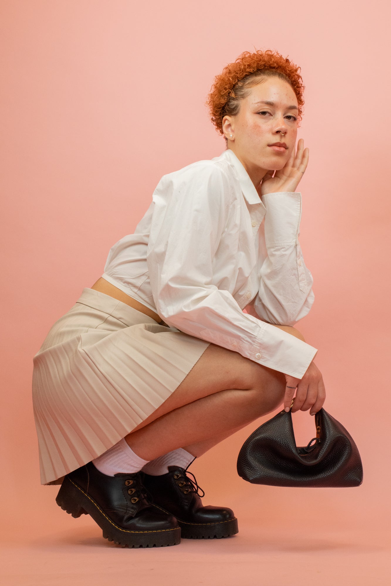 model kneeling down posing with slouchy handbag with convertible design in black leather