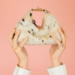 model with arms reached towards the sky holding up hair-on-hide leather crescent slouchy mini bag in speckled cowprint