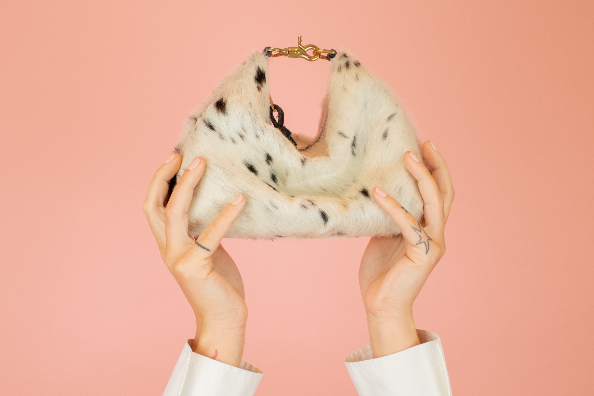 model with arms reached towards the sky holding up hair-on-hide leather crescent slouchy mini bag in speckled cowprint