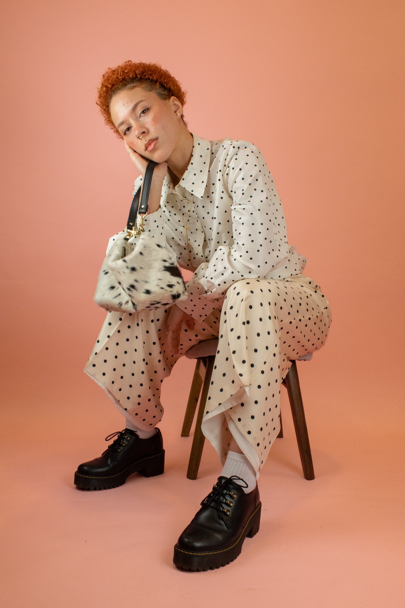 model wearing matching polka dot suit with gold lariat while holding up speckled hair-on-hide mini leather wristlet