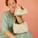 model posing with 2 off white leather handbags showing off there convertible design: part shoulder bag, part mini bag