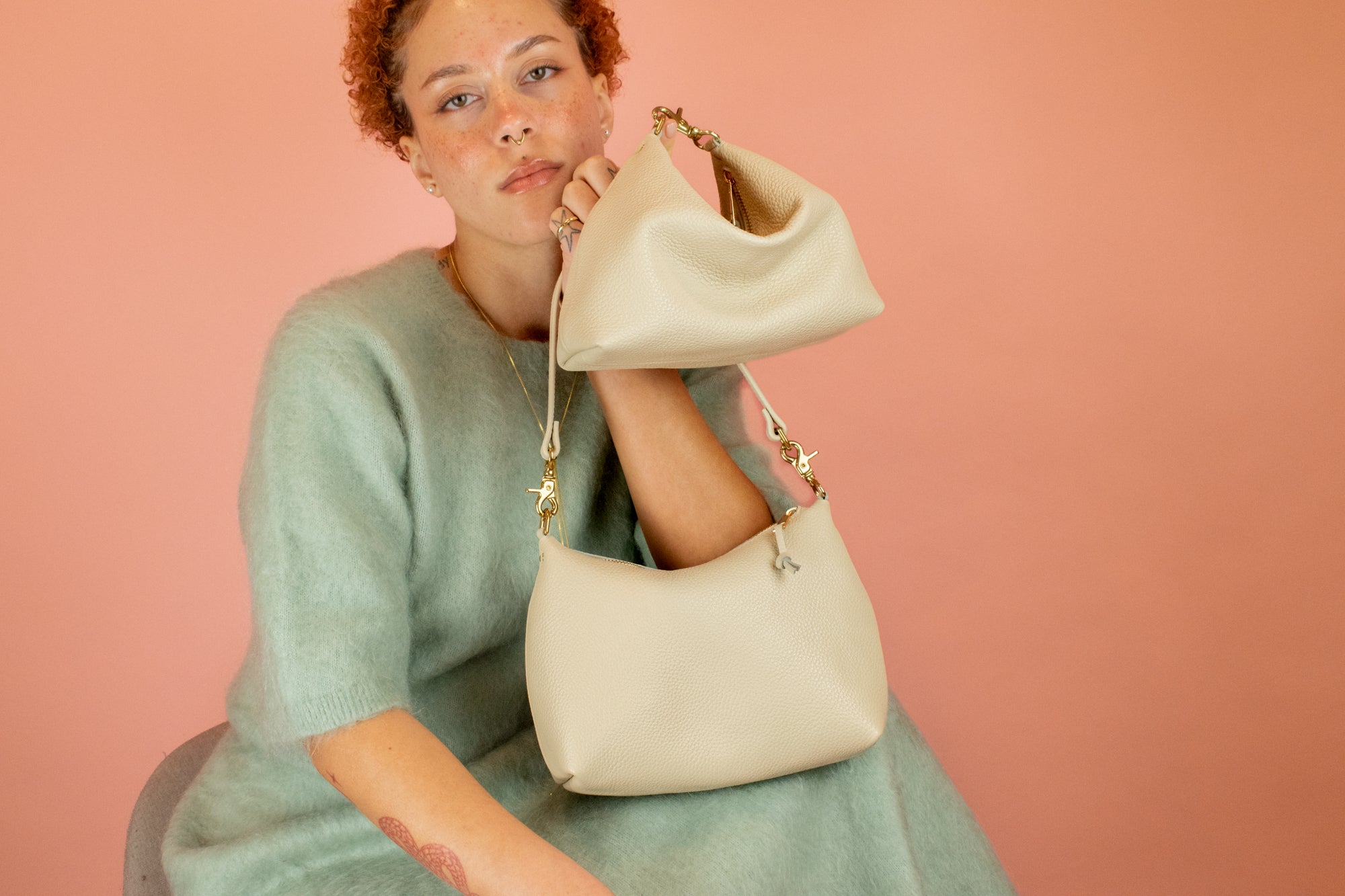 model posing with 2 off white leather handbags showing off there convertible design: part shoulder bag, part mini bag