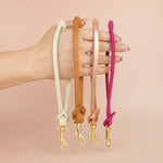 hands displaying four handmade modern leather keychain wristlets in bone white, caramel brown, rose gold, and barbie pink