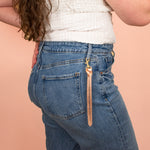 model wearing metallic rose gold leather keychain clipped onto belt loop