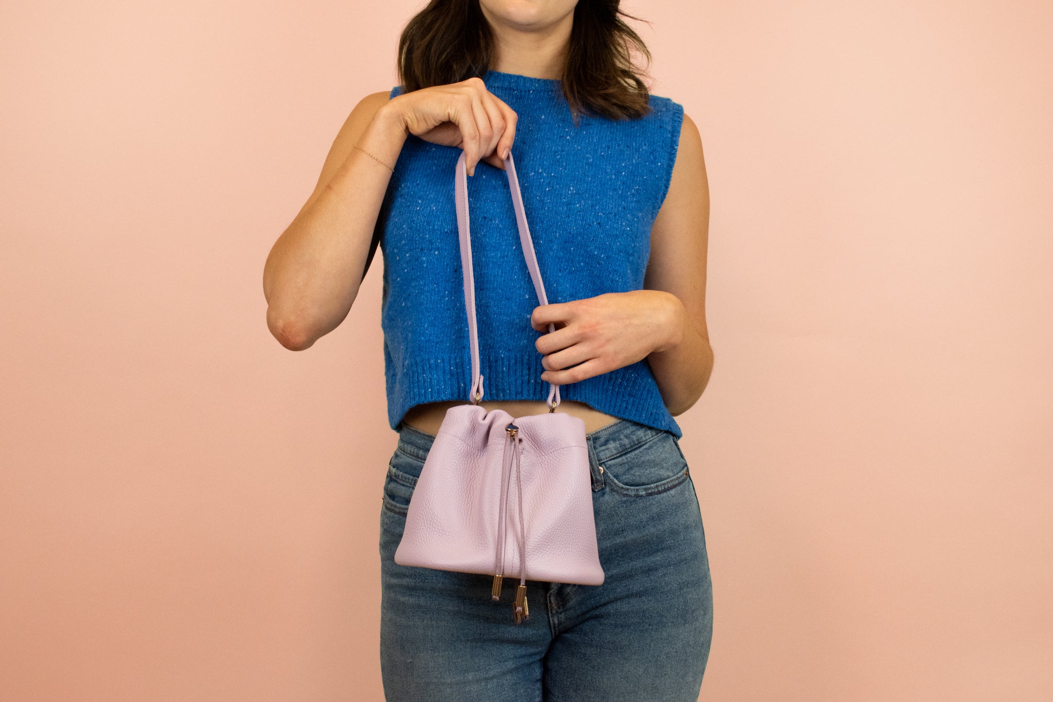 model holding up purple leather bucket bag with drawstring closure and gold hardware