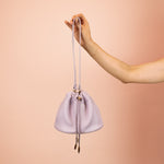 model holding out medium weight leather shoulder bag with adjustable strap and drawstring closure in lilac
