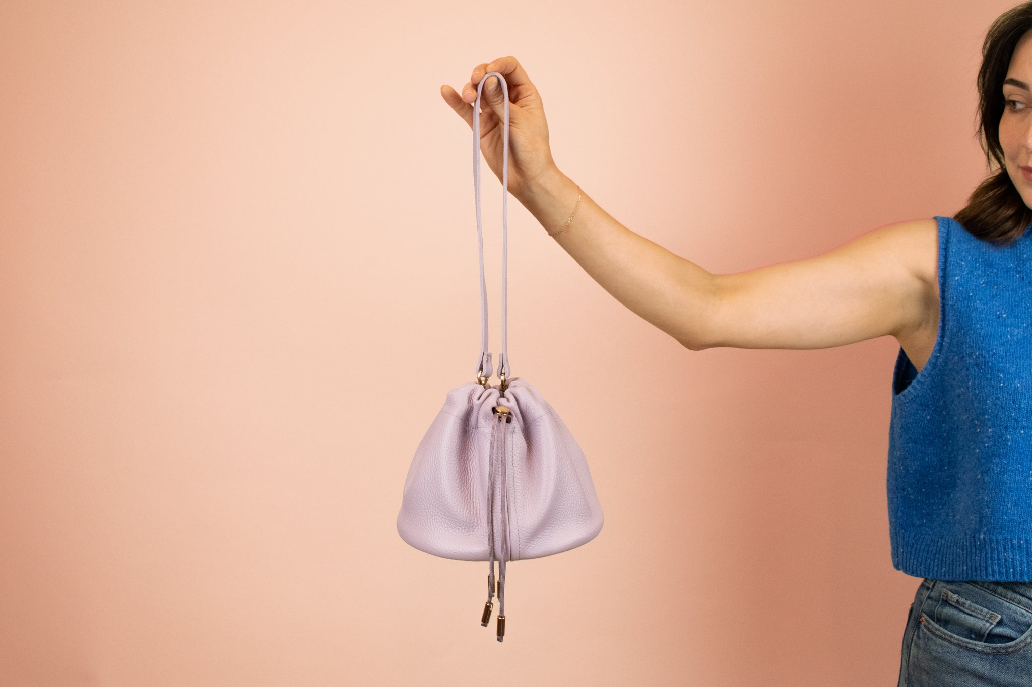model holding out medium weight leather shoulder bag with adjustable strap and drawstring closure in lilac