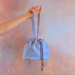 hand holding periwinkle drawstring shoulder bag