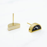 detail photo of 14k gold plated half moon earrings one laying faced down displaying gold plated post and the other front facing displaying black and white terrazo design