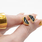 manicured hand holding pair of geometric black stone stud earrings