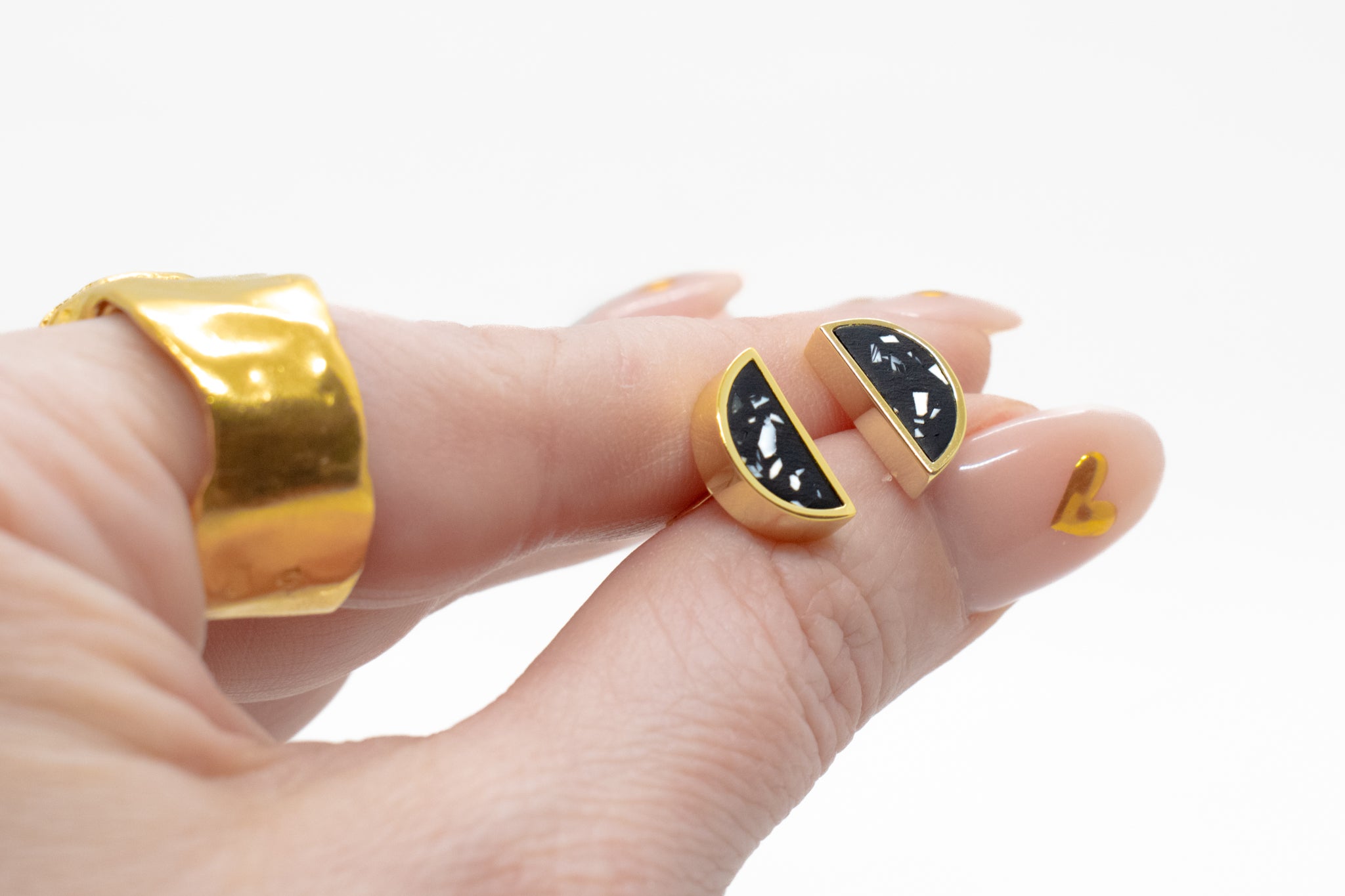 manicured hand holding pair of geometric black stone stud earrings