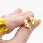 manicured hand holding pair of minimalist gold geometric earrings in multicolored terazzzo pattern