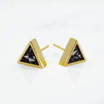 close up shot of gold triangle stud earrings with matte black clay and angular chips of white clay photographed on marble