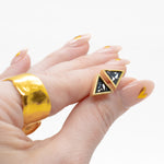 manicured hand holding pair of unique triangle stone earrings in 14k gold