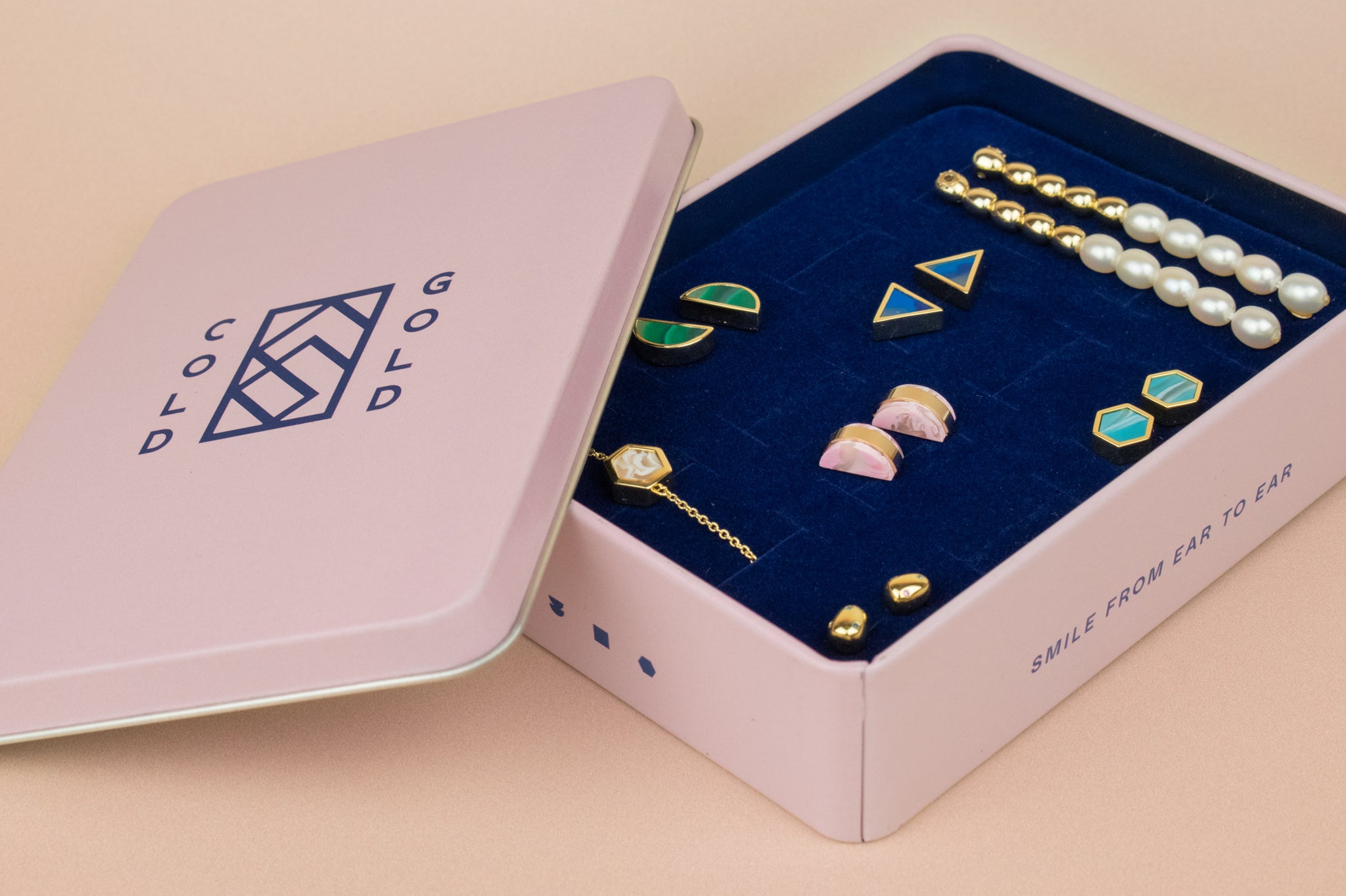 cold gold pink jewelry box with blue plush interior with 16 stud earring slots featuring various cold gold jewelry pieces designed in usa