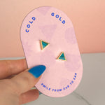 a hand holding a pill shaped pink card with a pair of marbled teal clay triangle earrings in gold