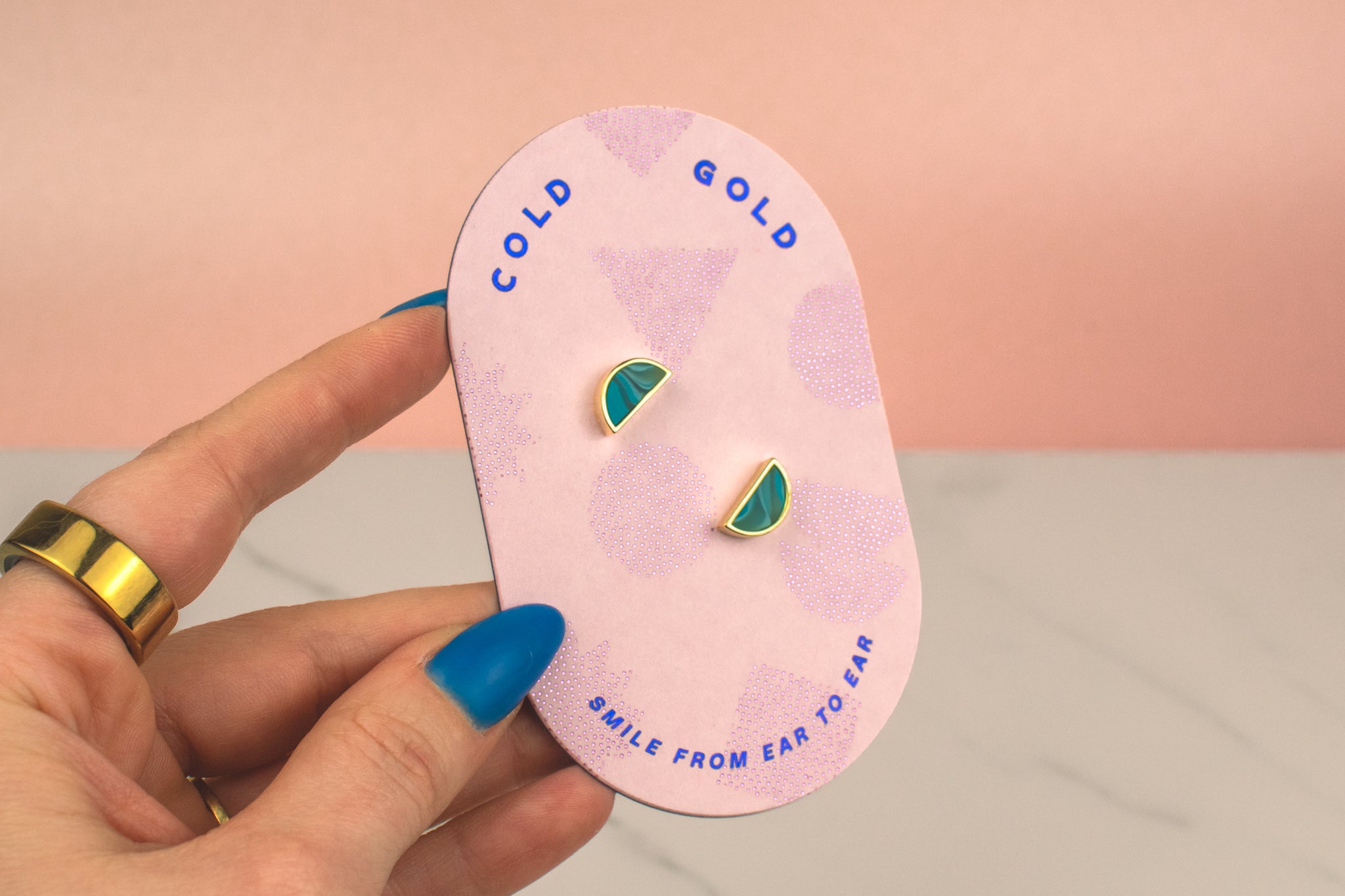a hand holding pink card with a pair of blue green crystal quartz triangle geo stud earring set on it