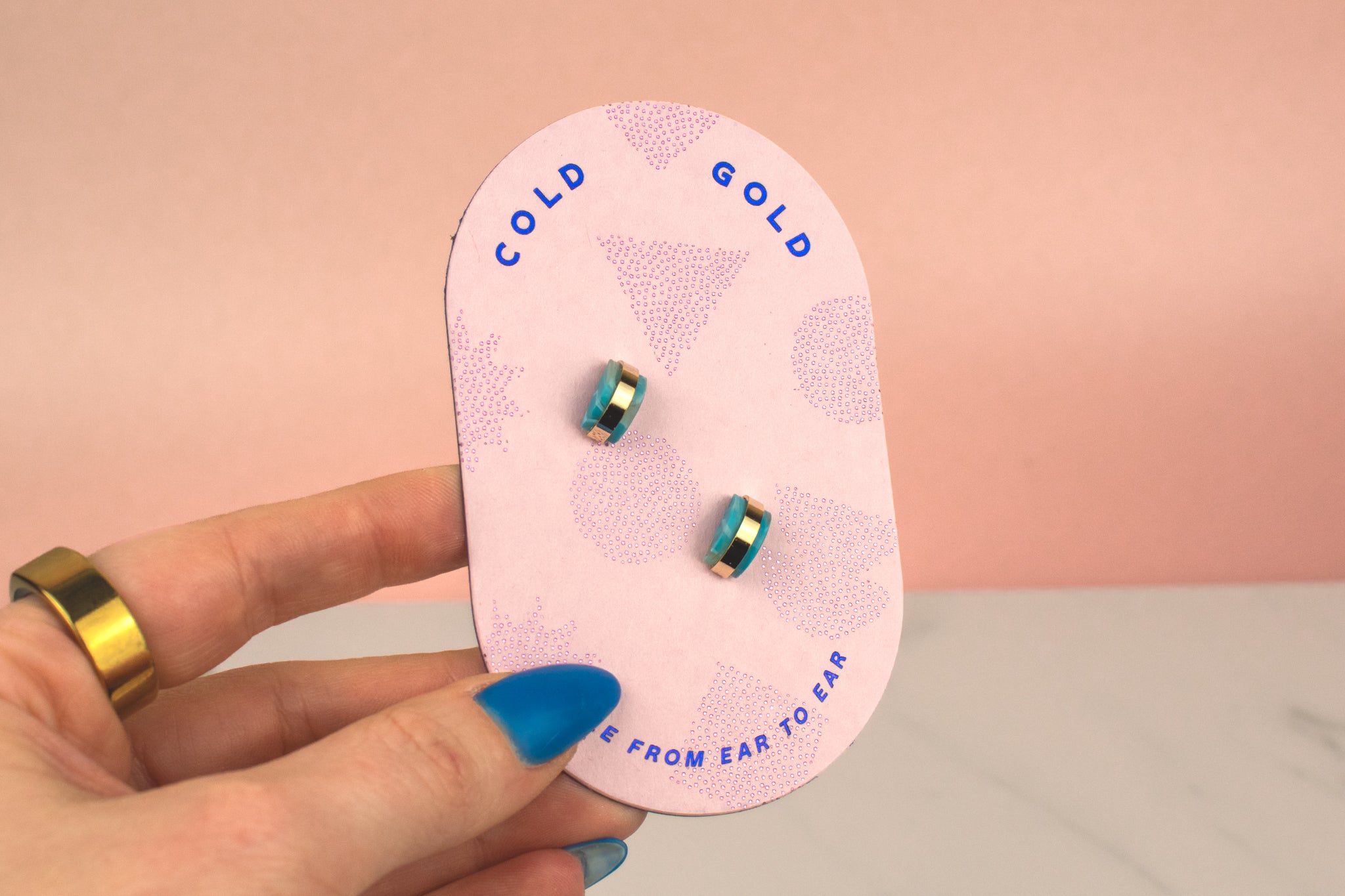 hand holding pink backer card displaying pair of aquamarine handmade clay gold hoop earrings