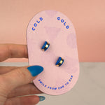 hand holding pink card displaying blue sapphire 14k gold earrings