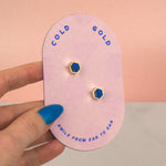 hand holding pink card displaying pair of blue sapphire modern hexagon honeycomb stud earrings with sterling silver posts