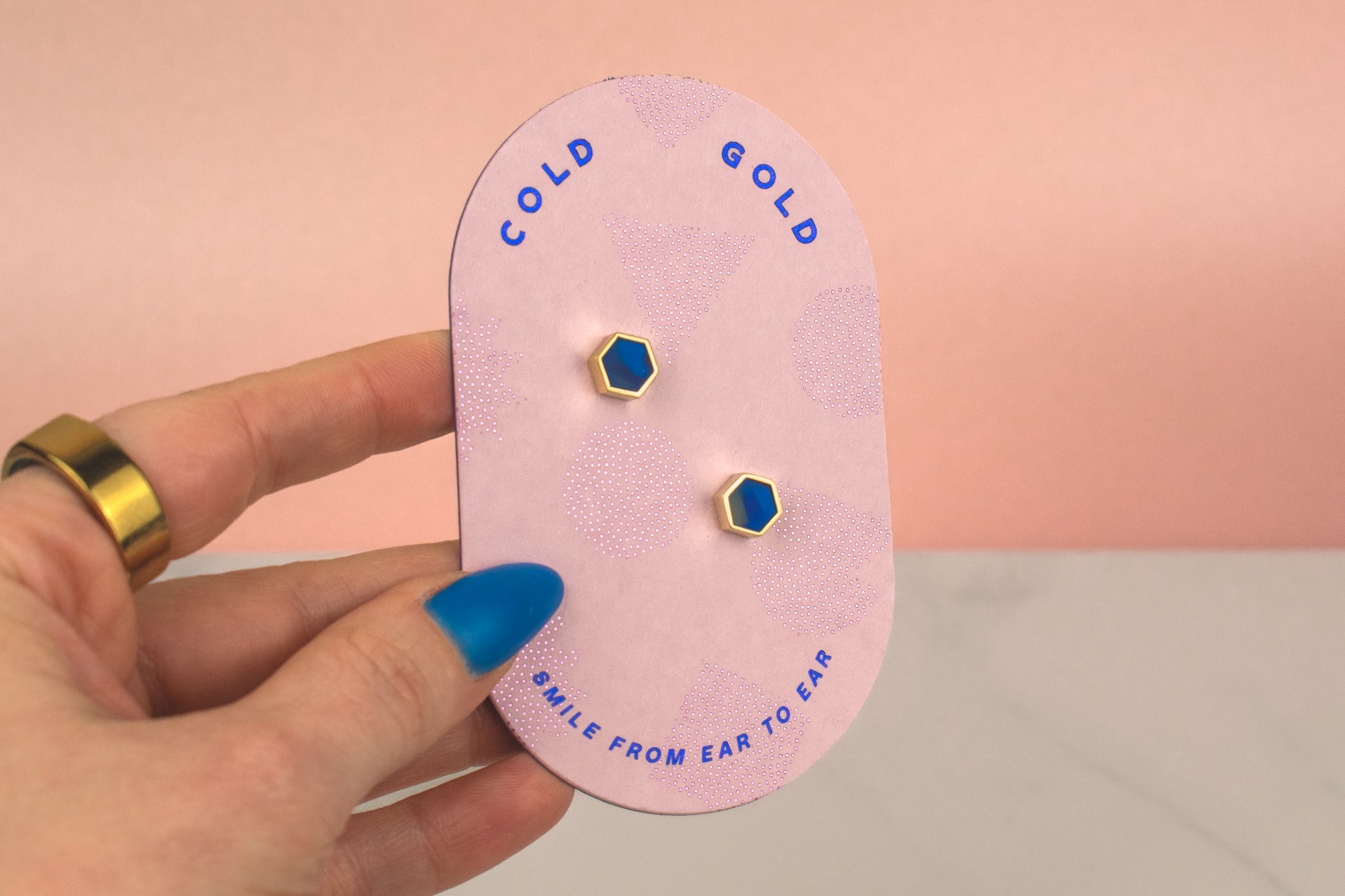 hand holding pink card displaying pair of blue sapphire modern hexagon honeycomb stud earrings with sterling silver posts
