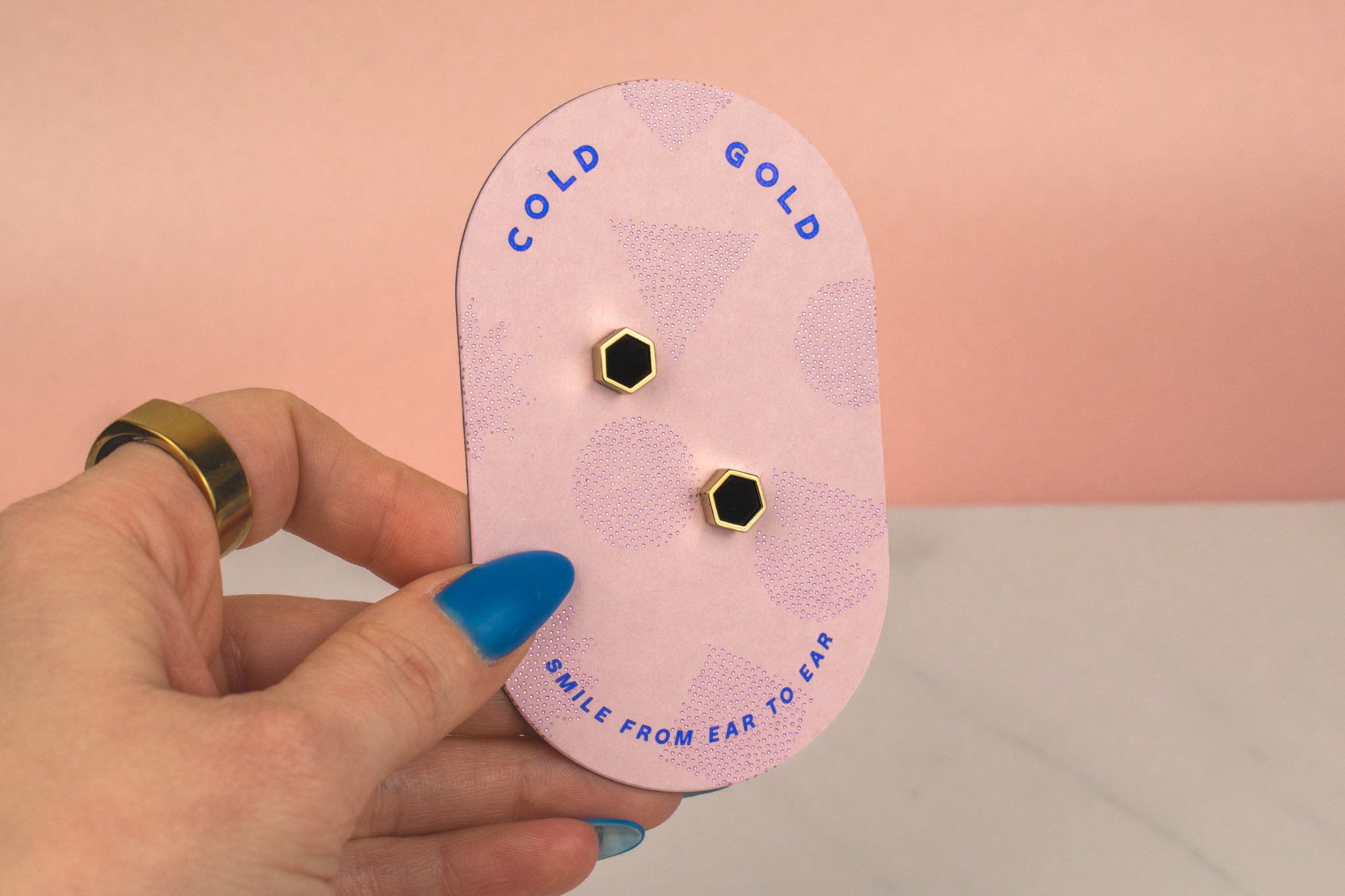 hand holding a pink backer card displaying pair of matte black handmade polymer clay gold hexagon stud earrings