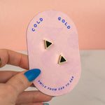 hand holding a pink packaging card with cold gold logo showing a pair of small triangle earrings black onyx and gold