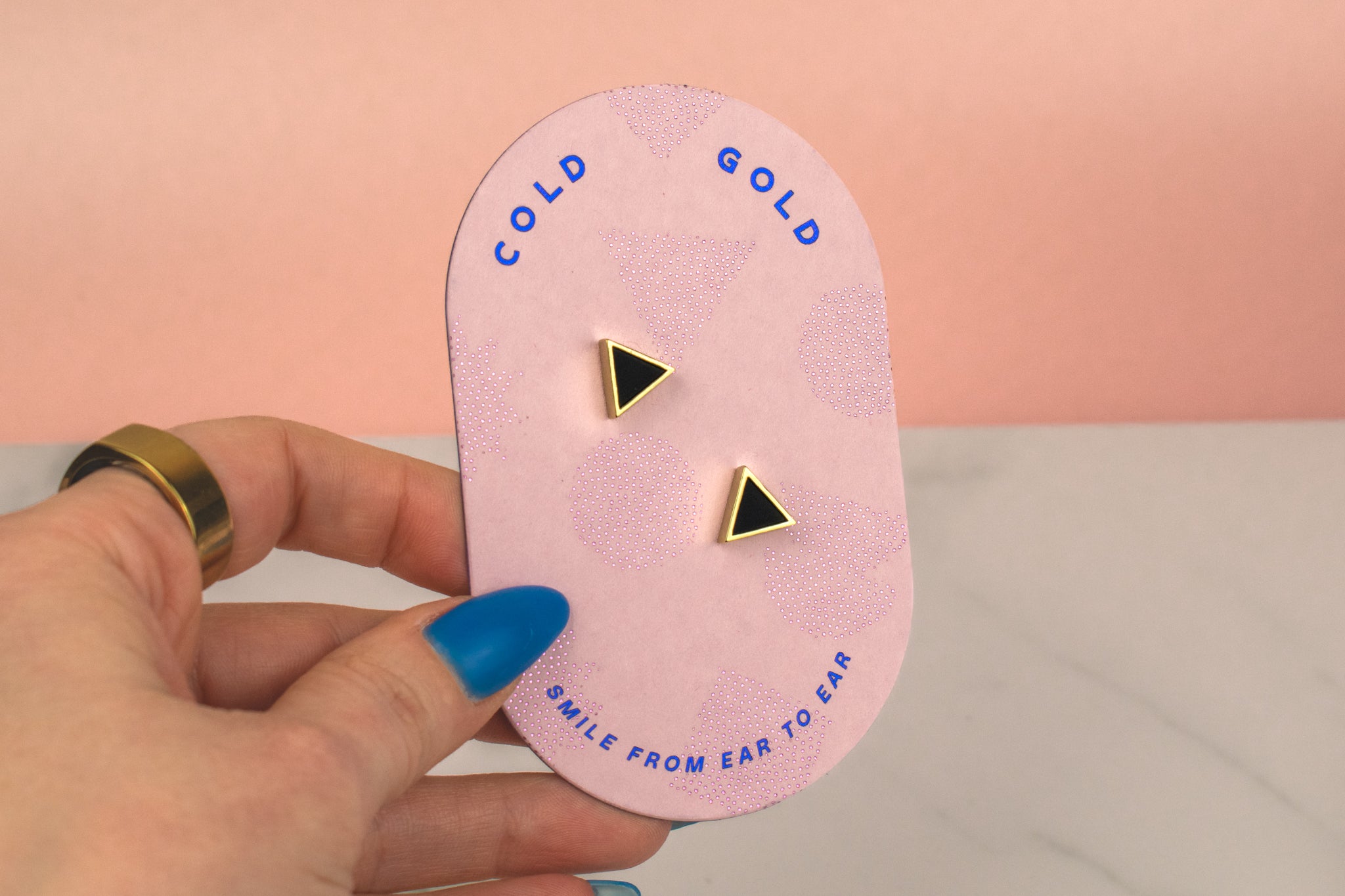 hand holding a pink packaging card with cold gold logo showing a pair of small triangle earrings black onyx and gold