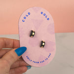 hand holding a light pink geometric card featuring the black and gold stud earring with a geometric and architectural style fit for all pierced ears