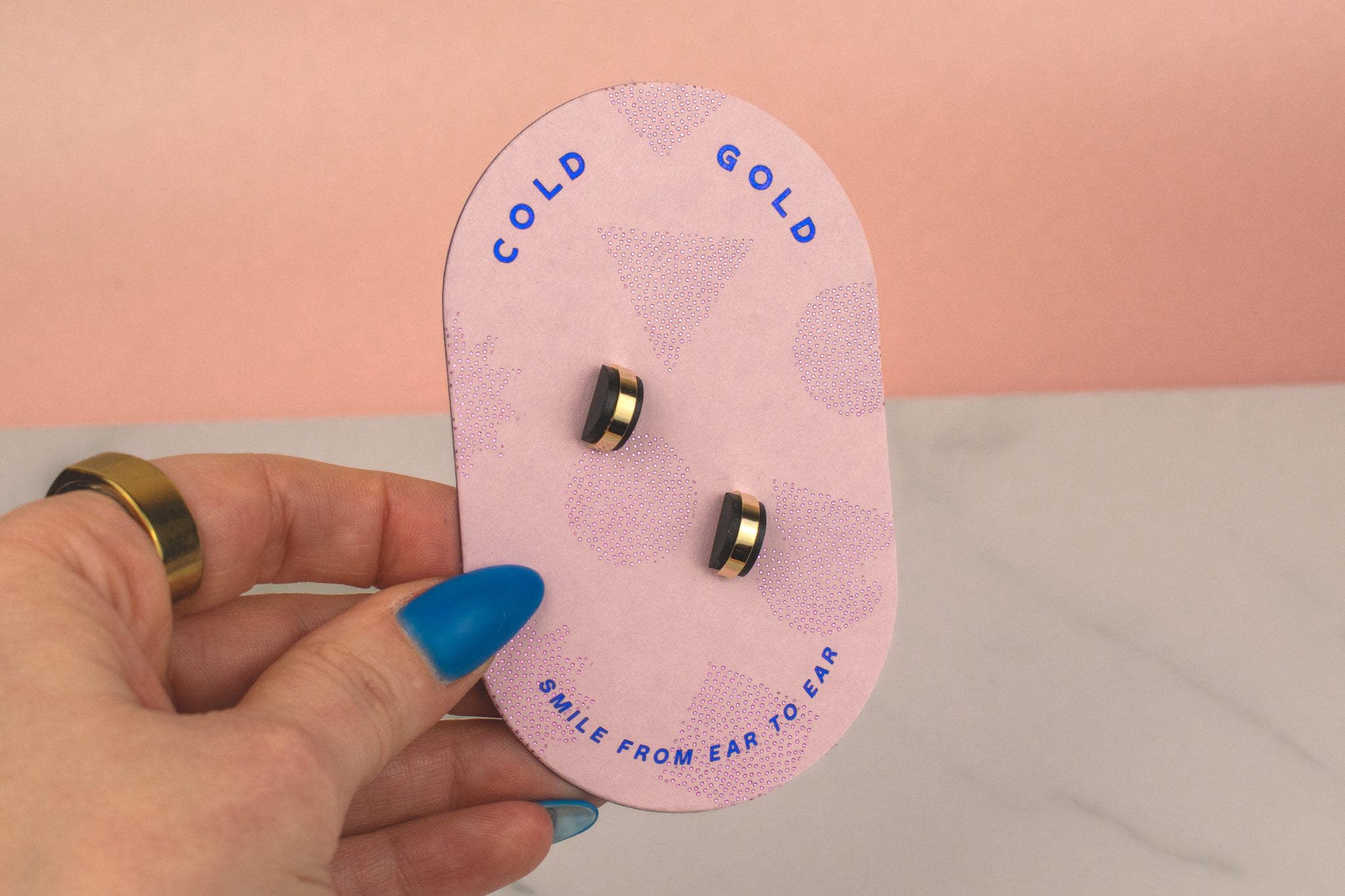 hand holding a light pink geometric card featuring the black and gold stud earring with a geometric and architectural style fit for all pierced ears