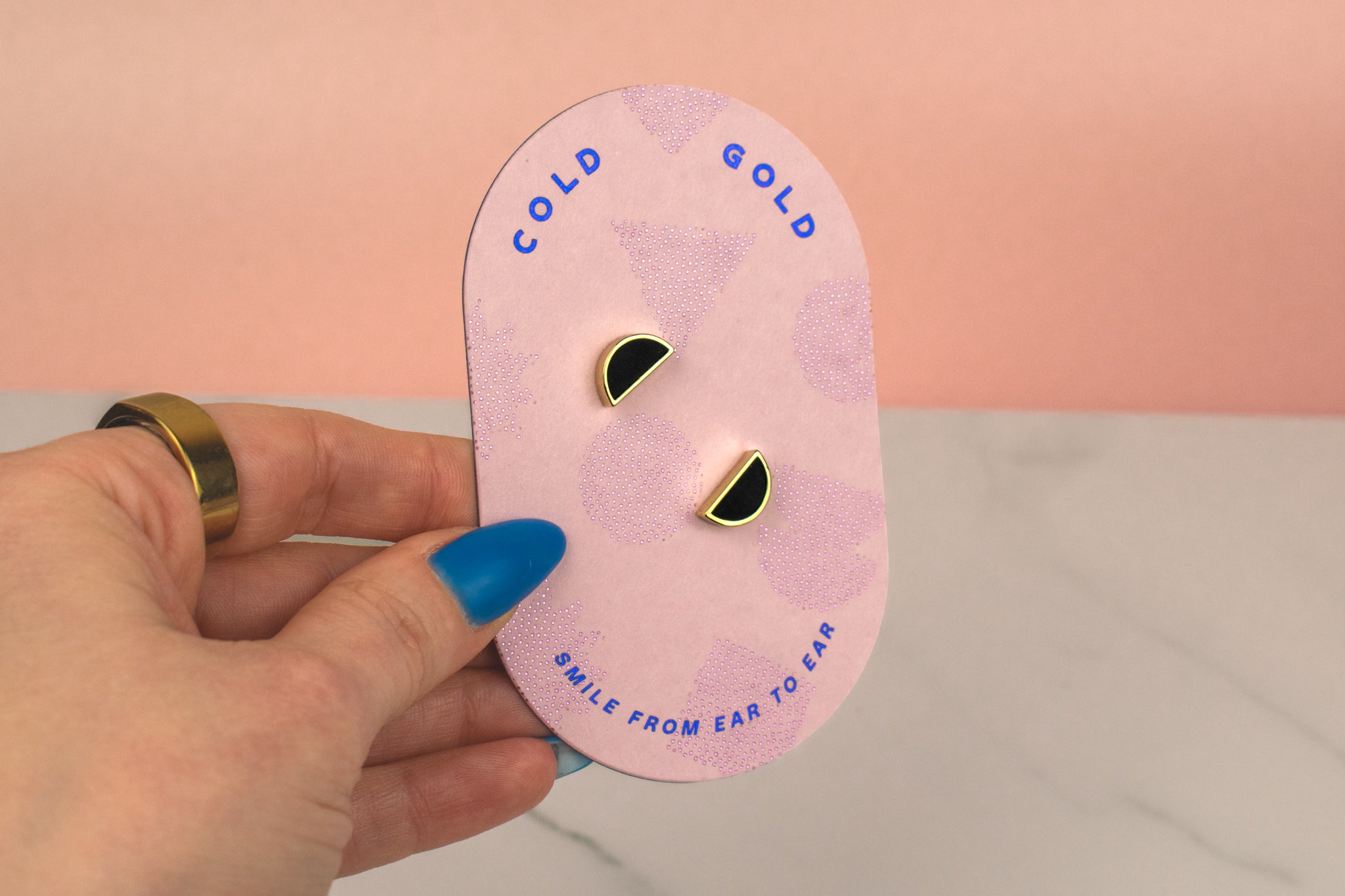 hand holding a set of three geometric earrings on geometric packaging showing 14k gold jewelry, half moon studs in black obsidian