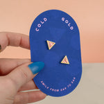 hand holding handmade geometric triangle stud earrings in cotton candy pink 14k gold plated on pink card