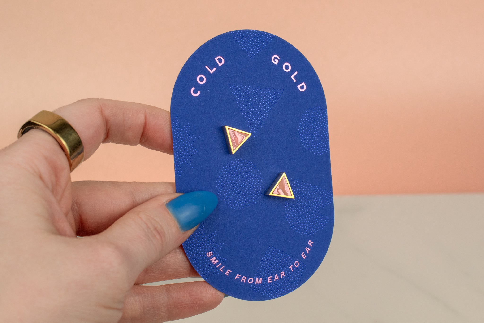 hand holding handmade geometric triangle stud earrings in cotton candy pink 14k gold plated on pink card
